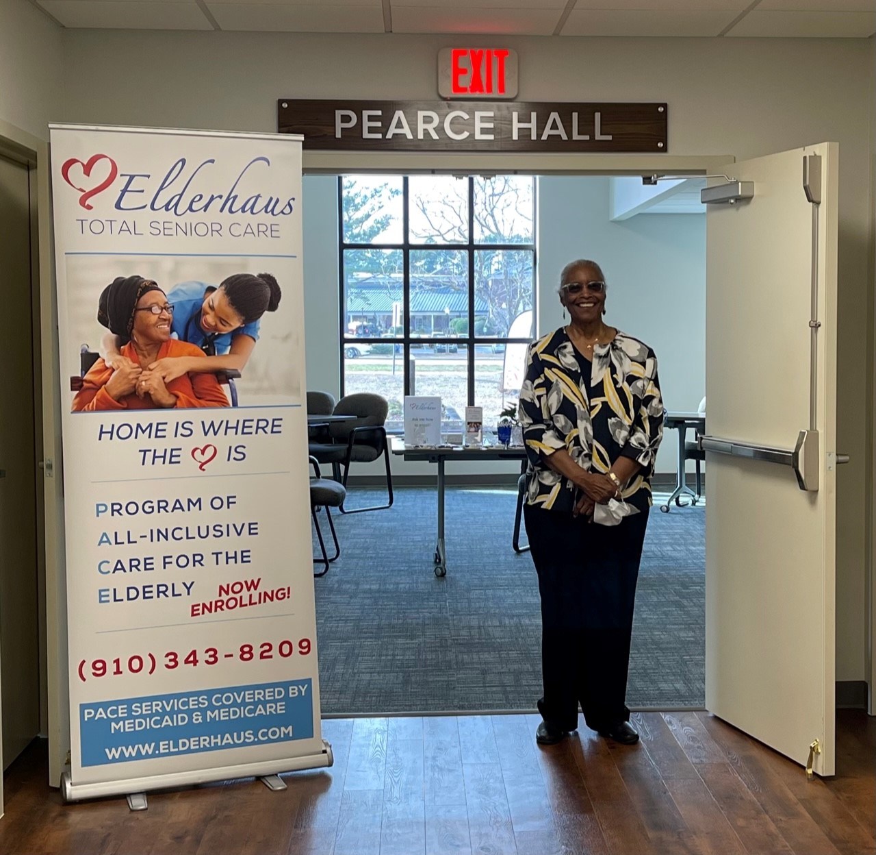 african american woman stands in doorway to a community room beside a standing banner